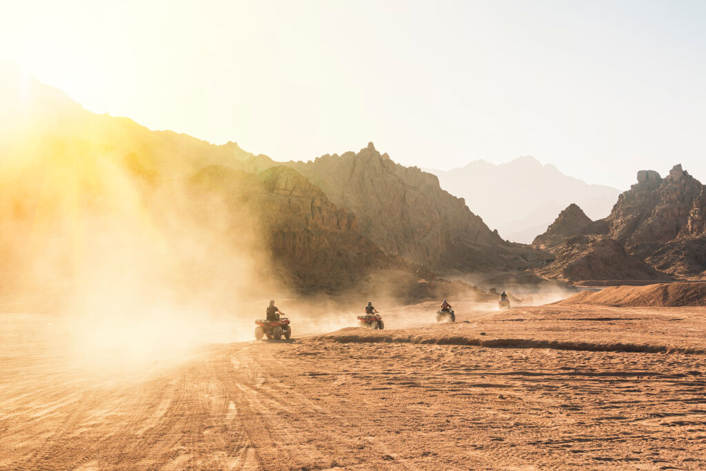 Wycieczki quadami - Grupa turystów na quadach na egipskiej pustyni. Dużo quadów w jeździe w kurzu na tle dzikiej pustyni. Zachód słońca na pustyni za górami. Rajd ATV.
